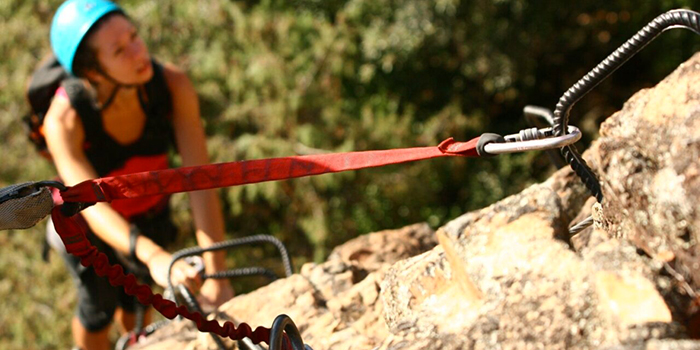 Image d'une femme dynamique grimpant sur un rocher, entourée de verdure, symbolisant l'effort physique et l'aventure extérieure.