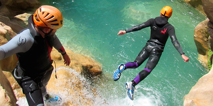 Photographie dynamique montrant deux aventuriers sautant dans une eau cristalline en pleine activité de canyoning, symbole d'adrénaline et de nostalgie des activités en plein air.