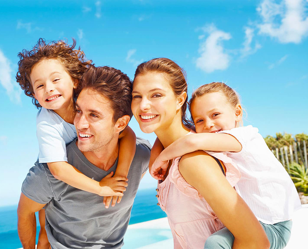 Image d'une famille heureuse à la plage, avec les enfants souriant sur le dos de leurs parents, évoquant bonheur et moments précieux en bord de mer.