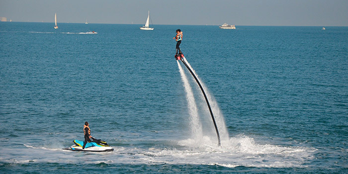 Un passionné de flyboard s'élève audacieusement au-dessus des vagues turquoise, entouré par l'excitation des jets d'eau.