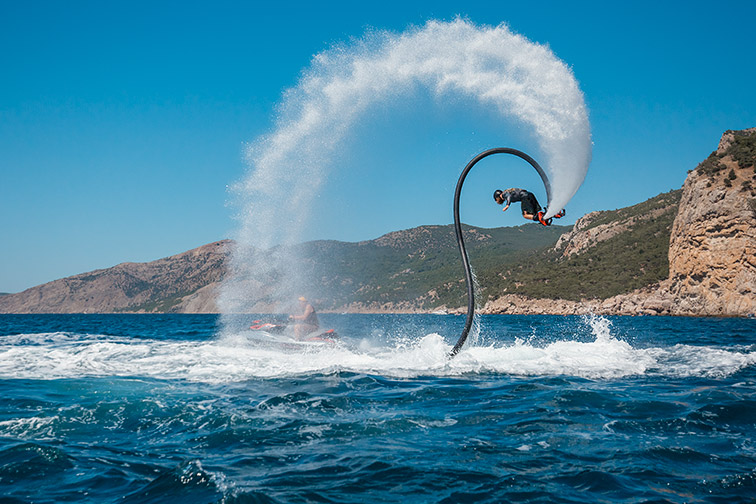 Moment dynamique capturé d'un homme en flyboard sur les vagues, se propulsant avec un jet d'eau et un fond montagneux pittoresque.