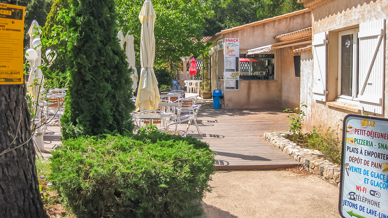 terrasse-ensoleillee-dun-snack-sous-les-arbres Terrasse d'un snack ombragée par de grands arbres, idéale pour se détendre avec un café ou une pizza en pleine nature, créant une ambiance estivale et conviviale.