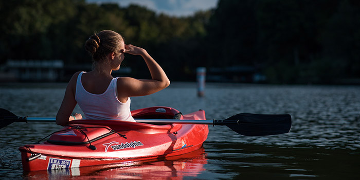 Une femme pagaye sereinement sur un lac au crépuscule, soulignant la symbiose entre nature et aventure, tandis que le soleil couchant illumine cette scène paisible.