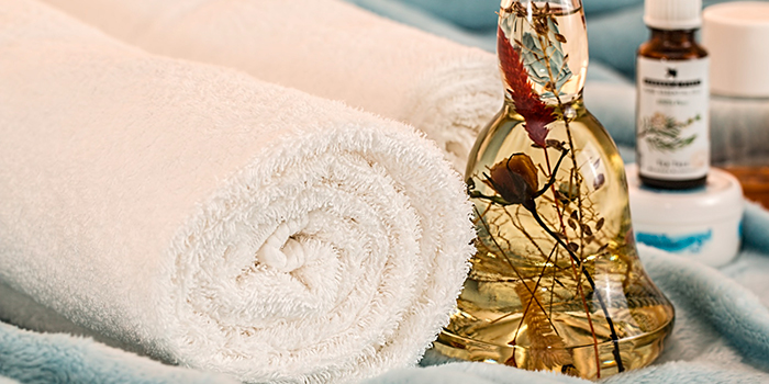 L'image représente une ambiance douce et relaxante avec une huile essentielle et des serviettes, idéale pour les soins personnels et le bien-être.