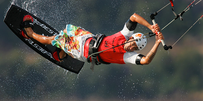 Photographie d'un sportif exécutant une figure de kitesurf acrobatique sur une mer scintillante, capturant l'énergie vibrante d'un sport nautique en été.