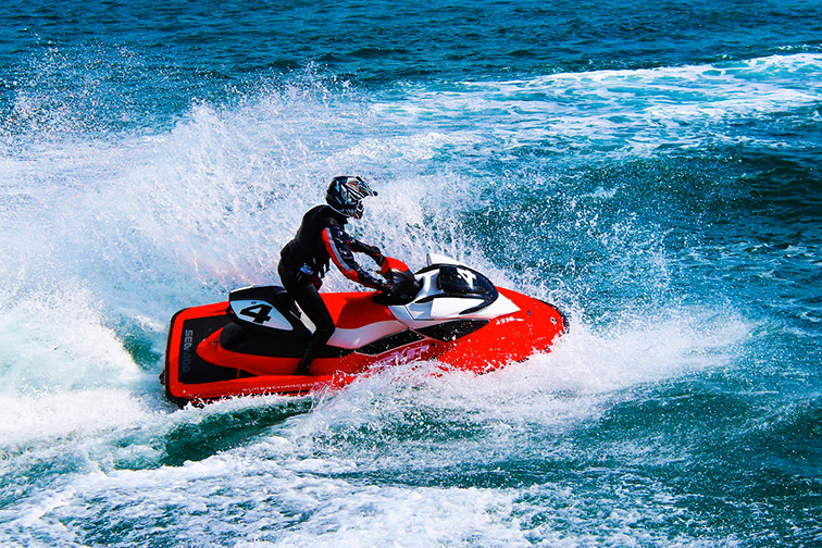 Un pilote de jet ski rouge navigue à grande vitesse sur des vagues éclatantes, illustrant l'aventure et l'excitation du sport nautique.