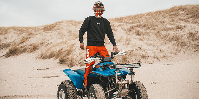 Passionné de motocross sur un quad bleu, prêt à explorer les dunes de sable sous un ciel ensoleillé, évoquant liberté et adrénaline.