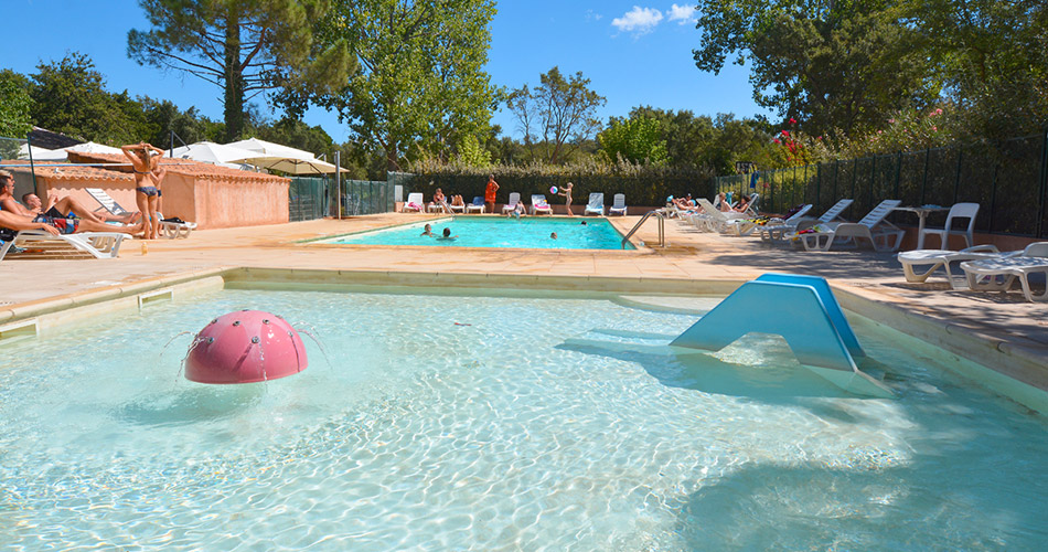 Cette image montre une piscine en plein air lors d'une journée ensoleillée, avec des familles profitant de diverses activités aquatiques, parsemées de moments de détente, parfait pour décrire une scène de vacances relaxantes et joyeuses.