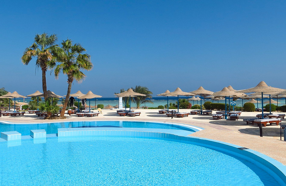 Scène idyllique d'une piscine avec palmiers et plage, parfaite pour se détendre sous le soleil.