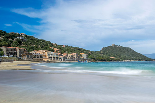 Paysage côtier pittoresque avec plage de sable fin, mer turquoise et maisons colorées sous un ciel dégagé, idéal pour des vacances relaxantes.