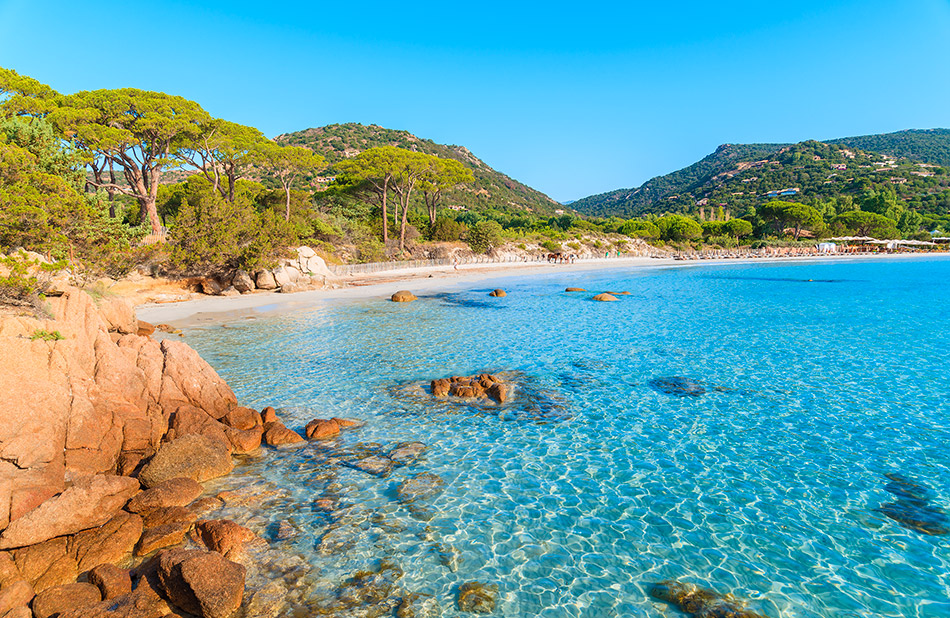 Image d'une plage aux eaux turquoise et cristallines avec des montagnes verdoyantes, idéale pour un sentiment de tranquillité et de vacances au bord de la nature.