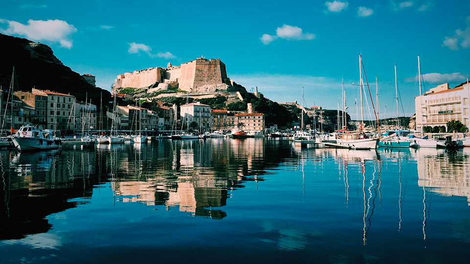 Vue panoramique du port de Bonifacio avec voiliers et falaises sur fond de ciel azur