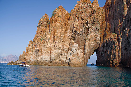 Rocher majestueux bordant l'océan Pacifique avec un petit bateau en navigation, évoquant sérénité et évasion.