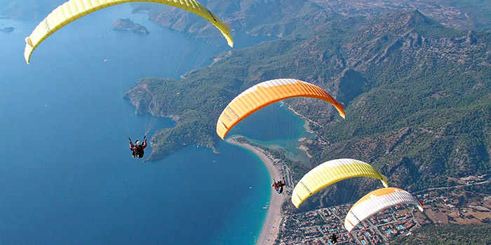 Scène aérienne de parachutisme au-dessus d'une plage ensoleillée, alliant adrénaline et admiration des vues côtières spectaculaires.