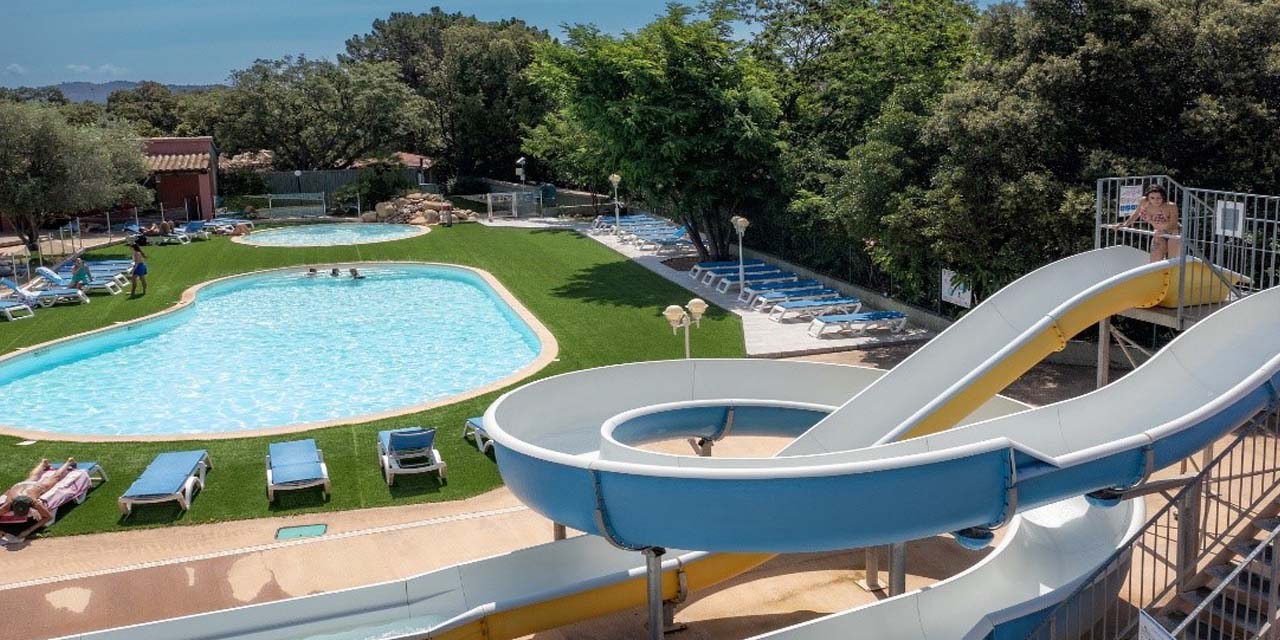 Scène estivale dans un camping familial avec toboggan pour enfants, piscine en plein air et espace de détente sous le soleil.
