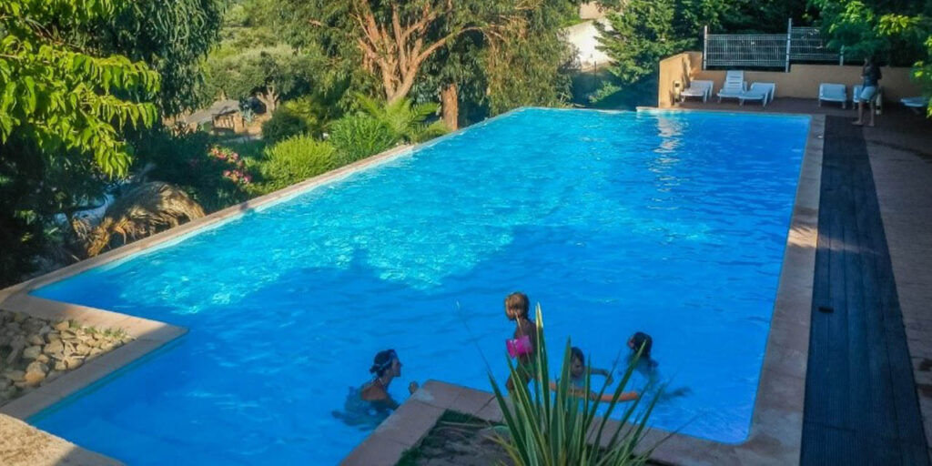 Enfants riant et jouant dans une piscine turquoise sous le soleil, entourés de verdure luxuriante, symbole de joie estivale et de détente en famille.