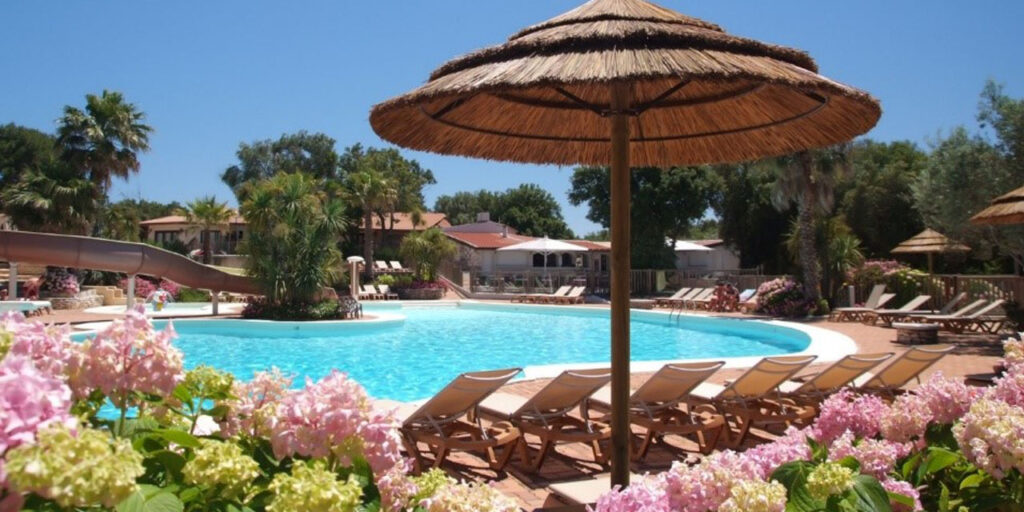Une belle piscine entourée de fleurs colorées et de palmiers sous un ciel bleu éclatant, invitant à la détente et au plaisir entre amis ou en famille.