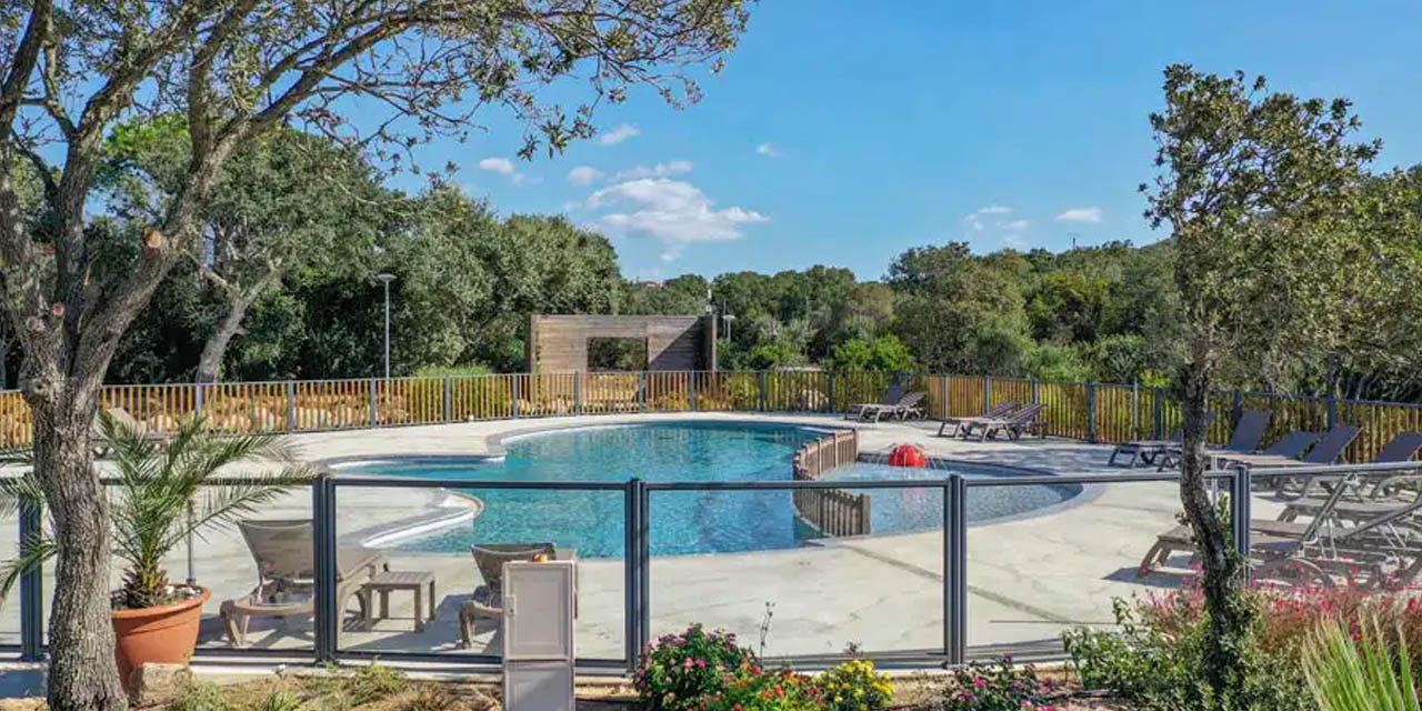 Image d'une piscine baignée de soleil, entourée de verdure et de chaises longues, parfaite pour des vacances détente.