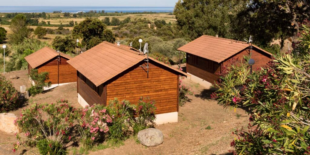 Vue panoramique sur des bungalows de camping en bois, nichés dans un cadre verdoyant avec une vue imprenable sur la mer, invitant à la détente et à des vacances en pleine nature.