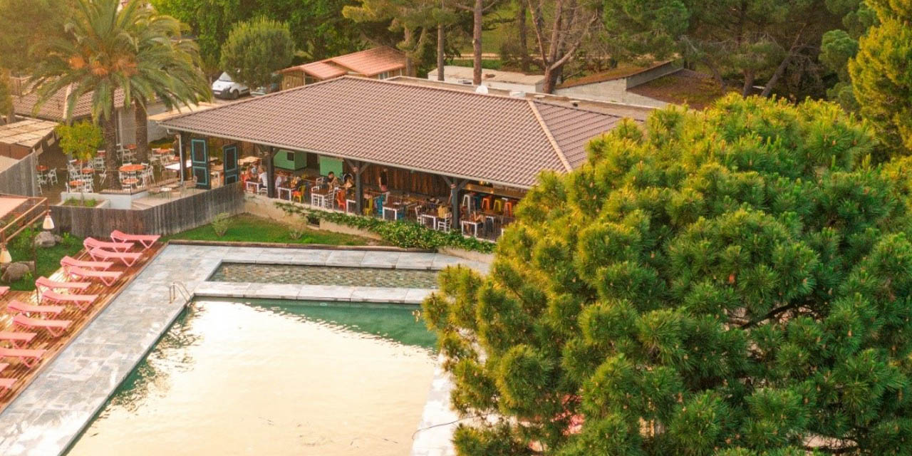 Vue aérienne d'un espace camping avec piscine, terrasse et arbres, magnifiant le cadre naturel pour une détente optimale.