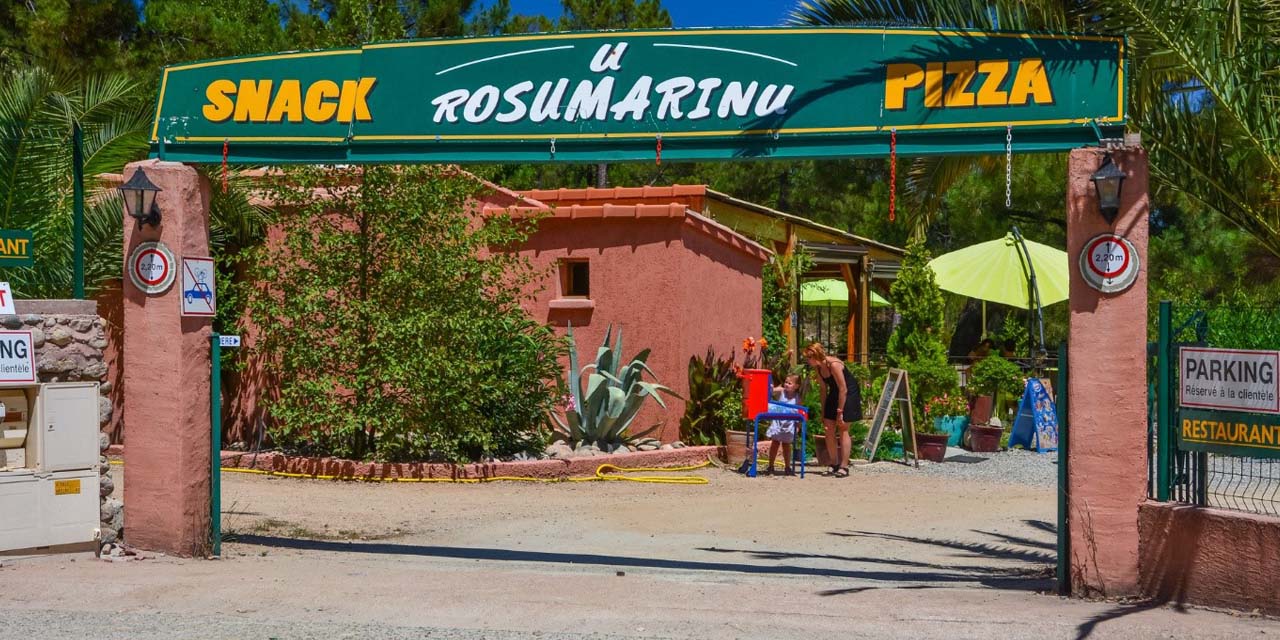 Terrasse estivale au Snack U Rosumarinu, où famille et amis se rassemblent pour partager des pizzas dans une ambiance conviviale entourée de verdure.