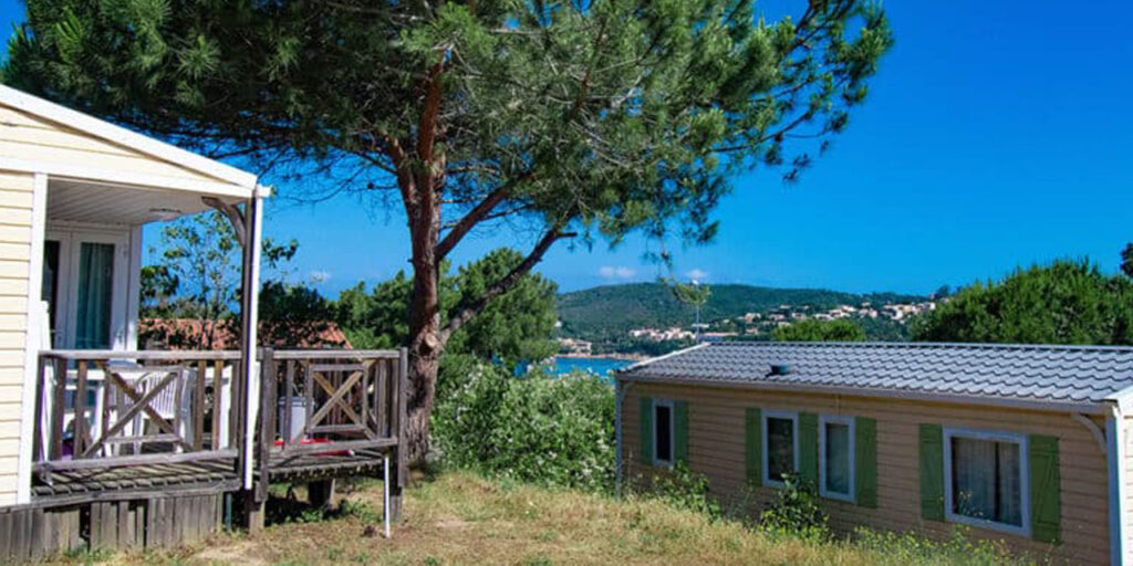 Maison de vacances avec terrasse en bois surplombant la mer, entourée de verdure pour un séjour relaxant en harmonie avec la nature.