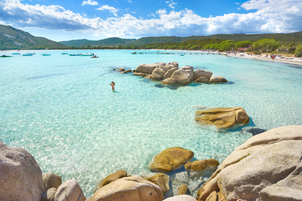 Plage de Santa Giulia aux eaux turquoises et rochers ensoleillés Plage de Santa Giulia avec eaux cristallines et rochers illuminés par le soleil, une destination idéale pour des vacances relaxantes sous un ciel bleu éclatant.