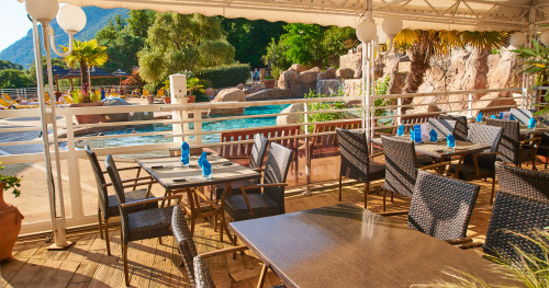 Terrasse de restaurant avec vue sur la piscine éclatante Terrasse de restaurant avec vue sur une piscine étincelante entourée de verdure et de palmiers, parfaite pour un repas convivial en extérieur.