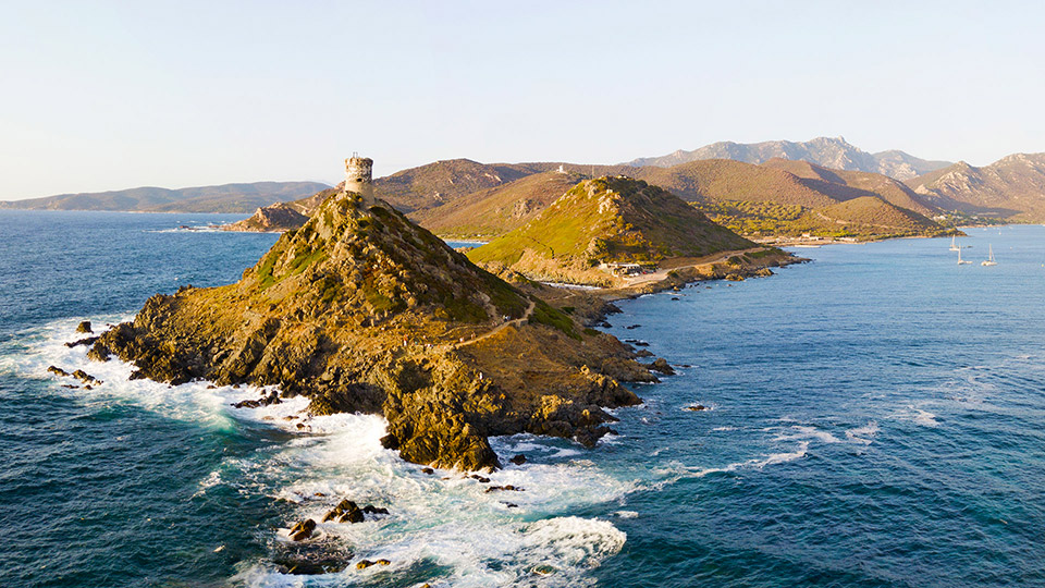 Texte alternatif (alt text) : Phare emblématique sur la côte d'Ajaccio, entouré de montagnes corses, baignées par le soleil couchant, offrant une vue panoramique paisible et spectaculaire.