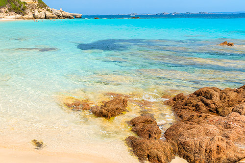 Photographie de la plage de Sperone avec des eaux turquoise éclatantes, rochers naturels et sable fin sous un soleil radieux, créant une ambiance sereine et idyllique.