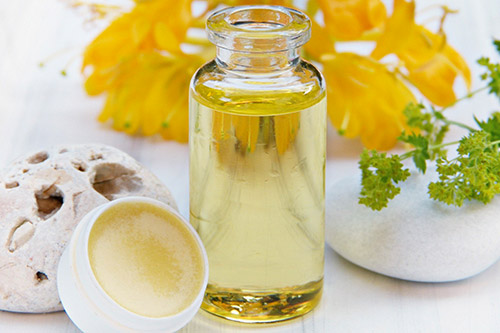 Dans une ambiance sereine, une bouteille d'huile essentielle transparente est entourée de pierres et de fleurs jaunes vibrantes, symbolisant le bien-être et l'équilibre. Idéale pour méditation et relaxation.